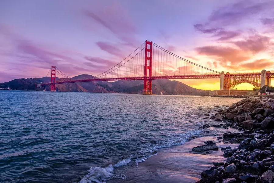 Le Golden Gate Bridge au coucher du soleil avec un ciel multicolore et la baie de San Francisco au premier plan.