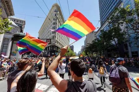 People walking in the San Francisco Pride parade wave rainbow flags.