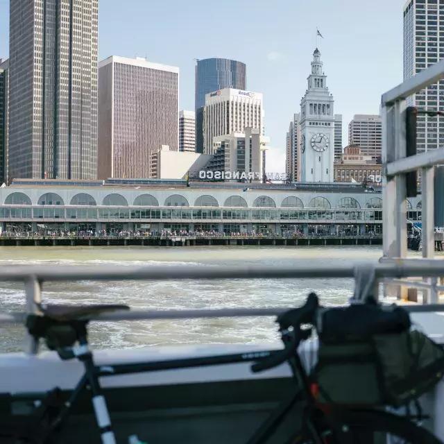 Bicicleta encostada em um trilho com o Ferry Building ao fundo.